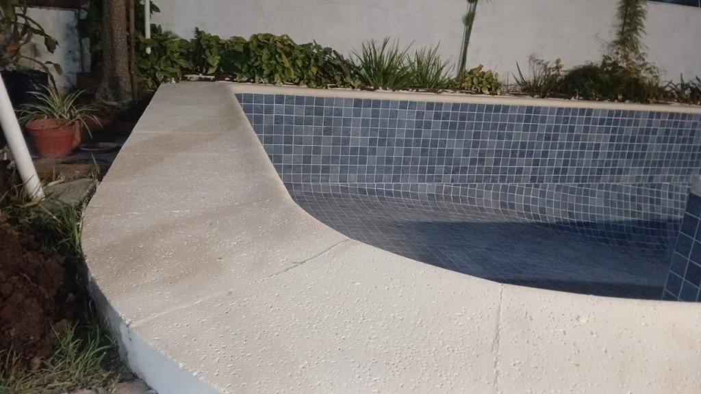 Borde de piedra y venecitas en esquina de piscina